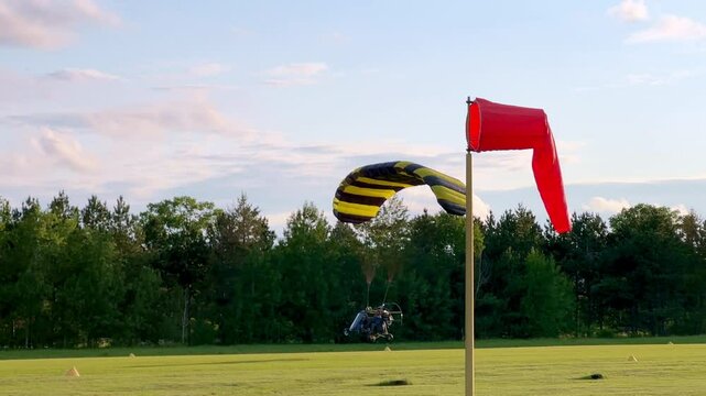 Ultralight powered parachute, with pilot and passenger, during take off from a grass runway in late afternoon light.