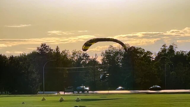 Ultralight powered parachute, with pilot and passenger, during a smooth touch and go landing and take off from a grass runway in late afternoon light.
