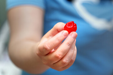 Woman's hand holding a large, bright red dried sweet cherry, showcasing natural snack and vibrant color