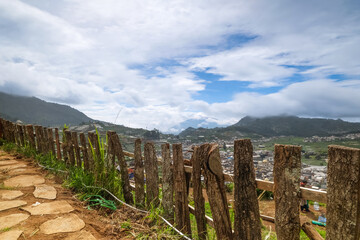 Scenic view of a rural landscape with wooden fence, mountains, and cloudy sky.