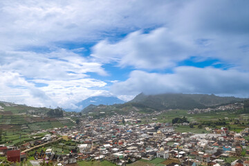 A scenic view of a town surrounded by lush green hills under a cloudy sky.