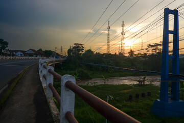 A serene sunset over a rural bridge with power lines and lush greenery.