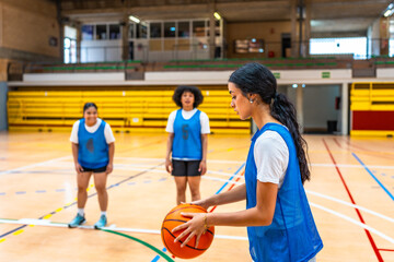 Female basketball player holding ball during training in gym with teammates