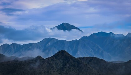 A landscape of mountains with a cloudy sky, the mountains are blue and the sky is blue.