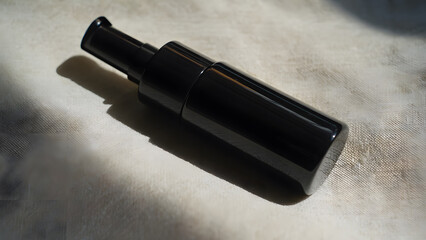 Glossy black cosmetic bottle on light fabric