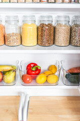 organized tidy decluttered pantry with matching clear jars of healthy ingredients like grains, legumes, spices, fruit and vegetables