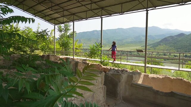 Female traveler sightseeing overlooking the preserved ruins of the King's Bath at Armaziskhevi site, surrounded by green hills and valley in Mtskheta region
