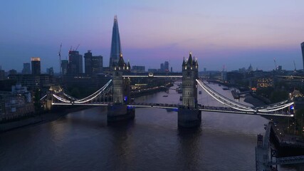 Aerial drone shots of Tower Bridge at twilight showcase Londons skyline against the Thames River, highlighting the citys beauty during enchanting evening hours that captivate all