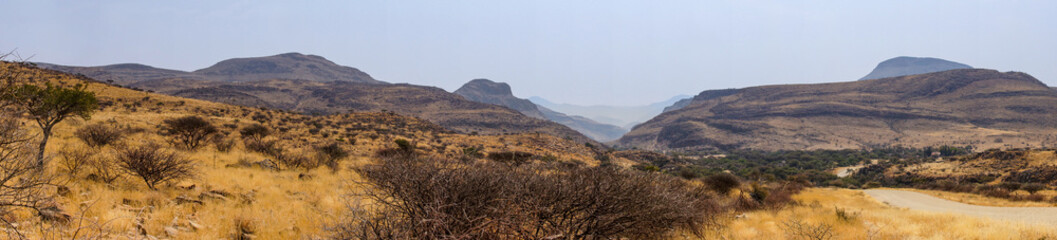 Panorama landscape of dry stony hills in Namibia and the road leading to Remhoogte Pass