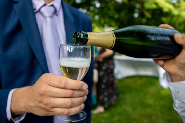 waiter serves a glass of champagne to a man in a suit outdoors on a party day
