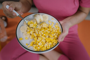 Young Asian woman holding a plate of corn kernels and sliced ​​bananas ready to eat as a fresh and healthy food or snack.