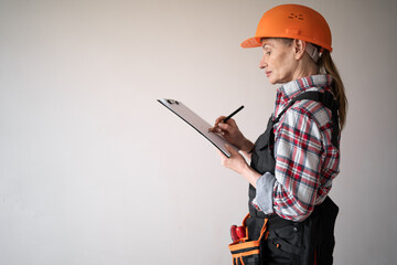 Female repairman or builder in yellow helmet writing notes in clipboard over white background....