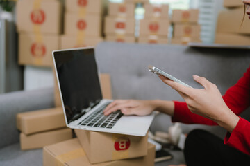 A person holds a yellow package next to a laptop and stacked boxes, indicating an active online shipping operation.