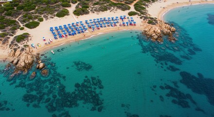 Aerial view of a beautiful sandy beach with rows of blue umbrellas and sunbathers by the turquoise sea, featuring clear water and rocky shores. Perfect scene for a summer vacation or travel theme.