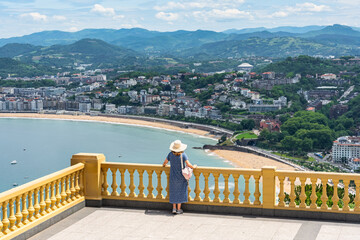Obraz premium Tourist woman leaning out of a large balcony with stunning views of the bay of San Sebastian, Basque Country.