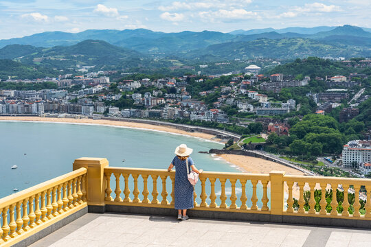 Tourist woman leaning out of a large balcony with stunning views of the bay of San Sebastian, Basque Country.