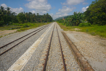 Railroad track bordered by trees on a summer day in Malaysia countryside.