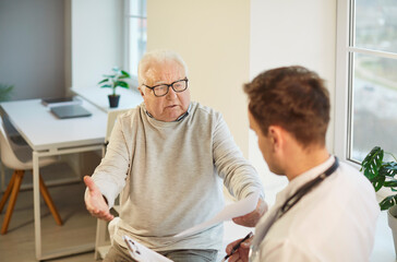 Obraz premium Elderly man complains about health problems while having appointment with doctor, asks for advice and prescription, gets consultancy, looking frustrated as cannot overcome serious disease