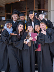 Happy students of different nationalities in graduation gowns hold their diplomas.