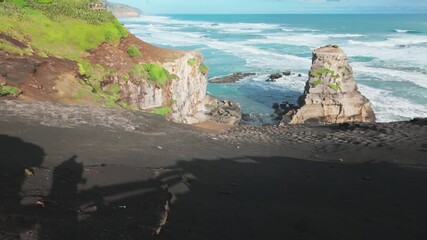 Black sand beach and cliffs overlook a sea stack and the ocean waves on the rugged west coast of Muriwai, Auckland, New Zealand - Powered by Adobe