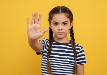 Young girl with braids holding her hand up in a stop gesture against a yellow background