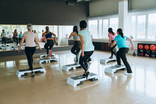 Group fitness class using steppers in gym for cardio exercise active lifestyle and wellness - Powered by Adobe