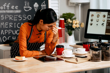 A young Asian female barista in a striped apron and orange shirt stands in a cozy modern café,...