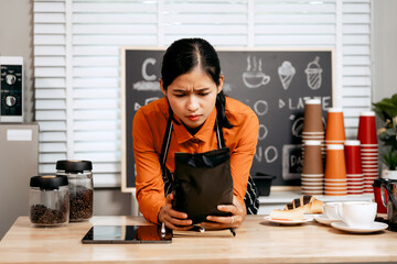 A young Asian female barista in a striped apron and orange shirt stands in a cozy modern café,...