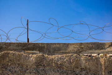 Concrete wall with barbed wire against a clear blue sky. Security barrier.