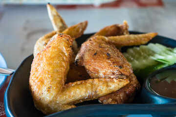 Close-up of crispy fried chicken wings served with sliced cucumbers and dipping sauce on a black plate