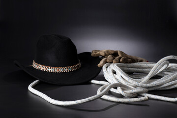 Cappello da cowboy, corda e guanti su sfondo nero.