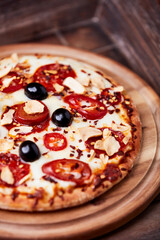 Pizza with salami and mozzarella cheese, jalapeno pepper and black olives. Wooden background. Soft focus. Close up.	