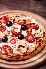 Pizza with salami and mozzarella cheese, jalapeno pepper and black olives. Wooden background. Soft focus. Close up.	