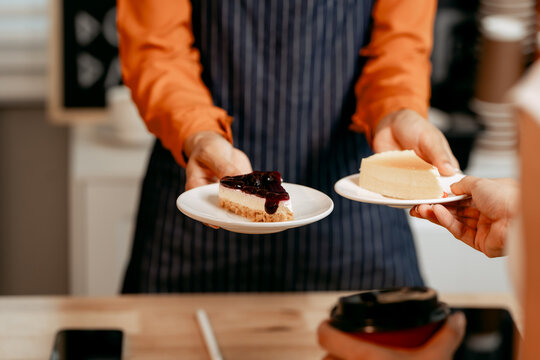 A young Asian female barista in modern cafe assists woman customer ordering latte, fresh coffee beans, dark roast, croissant, completing the purchase with mobile payment at the POS using QR code.