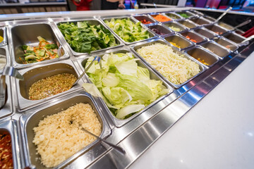 A variety of fresh ingredients displayed in a salad bar with stainless steel containers and colorful vegetables.