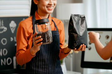 A young Asian female barista in modern cafe assists woman customer ordering latte, fresh coffee beans, dark roast, croissant, completing the purchase with mobile payment at the POS using QR code.