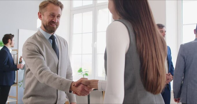 Positive businessman and businesswoman shake hands in an office after a successful business deal. Teamwork, collaboration, partnership, and agreement in a professional environment.