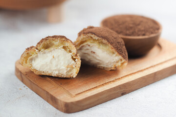 delicious cream puffs filled with smooth vanilla cream and dusted with cocoa powder. The dessert with a bowl of cocoa powder in the background. Perfect for dessert menus, or food blogs.