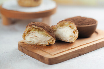cream puffs sliced in half, showing rich vanilla cream filling, topped with cocoa powder. The texture of the cream puff pastry and the smoothness of the cream filling are clearly visible.