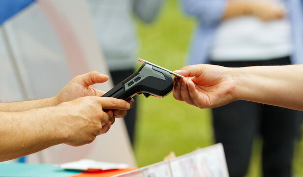 Contactless payment transaction with a card reader being used by two individuals outdoors, emphasizing modern technology and convenience in electronic transactions.