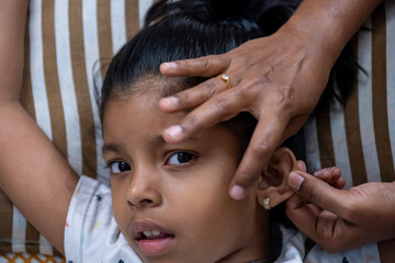 Child receiving ear piercing by skilled adult hands