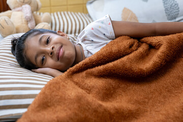 Child relaxing on bed under cozy blanket indoors
