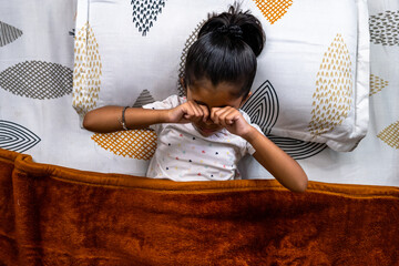 Child waking up and rubbing eyes in cozy bed