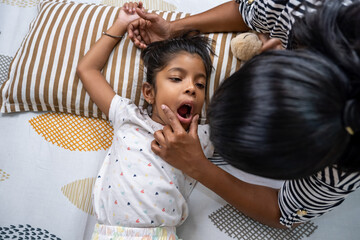 Child yawning while parent plays on a cozy bed