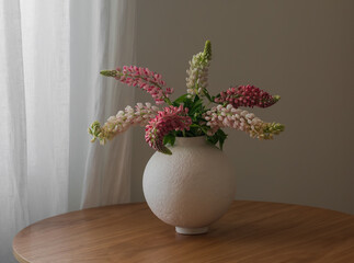Bouquet of lupines in a round ceramic vase on a wooden table