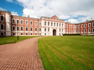 Obraz premium Huge court yard of Jelgava palace with well looked after grass lawn and neat footpaths, blue cloudy sky. Popular city landmark and tourist attraction. Warm sunny day. Latvia travel and tourism.