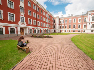 Girl on a bench in huge court yard of Jelgava palace with well looked after grass lawn and neat...