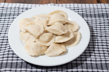 A plate of dumplings sits on a checkered cloth. The dumplings are white and arranged in a neat pile, Popular East European food. Simple easy meal.