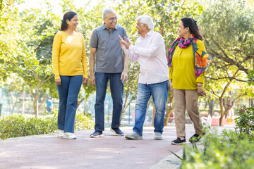Group of happy indian senior men and women laughing and walking together in summer park. Retirement life, retired people enjoying in garden