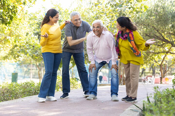 Group of happy indian senior men and women laughing and walking together in summer park. Retirement life, retired people enjoying in garden